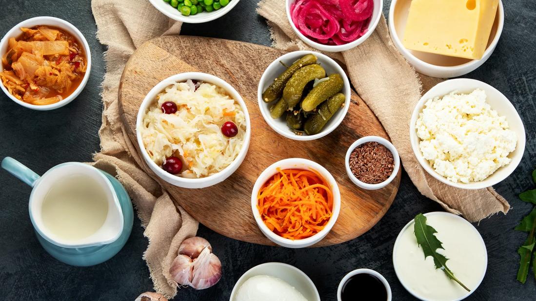 Variety of fermented probiotic foods including sauerkraut, pickles, kefir, and yogurt arranged on a wooden board