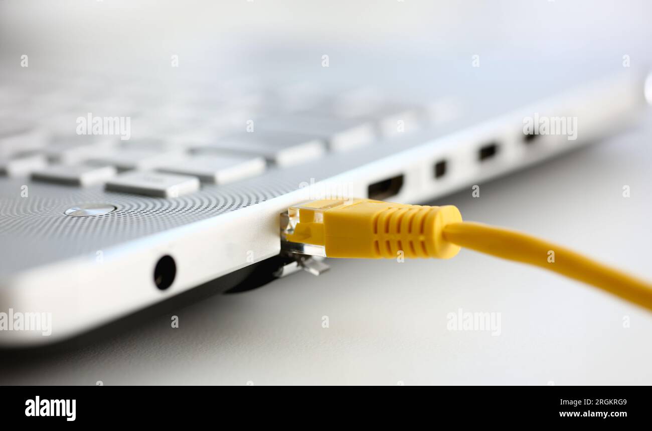 Close-up side angle of a yellow ethernet cable plugged into the port of a white laptop