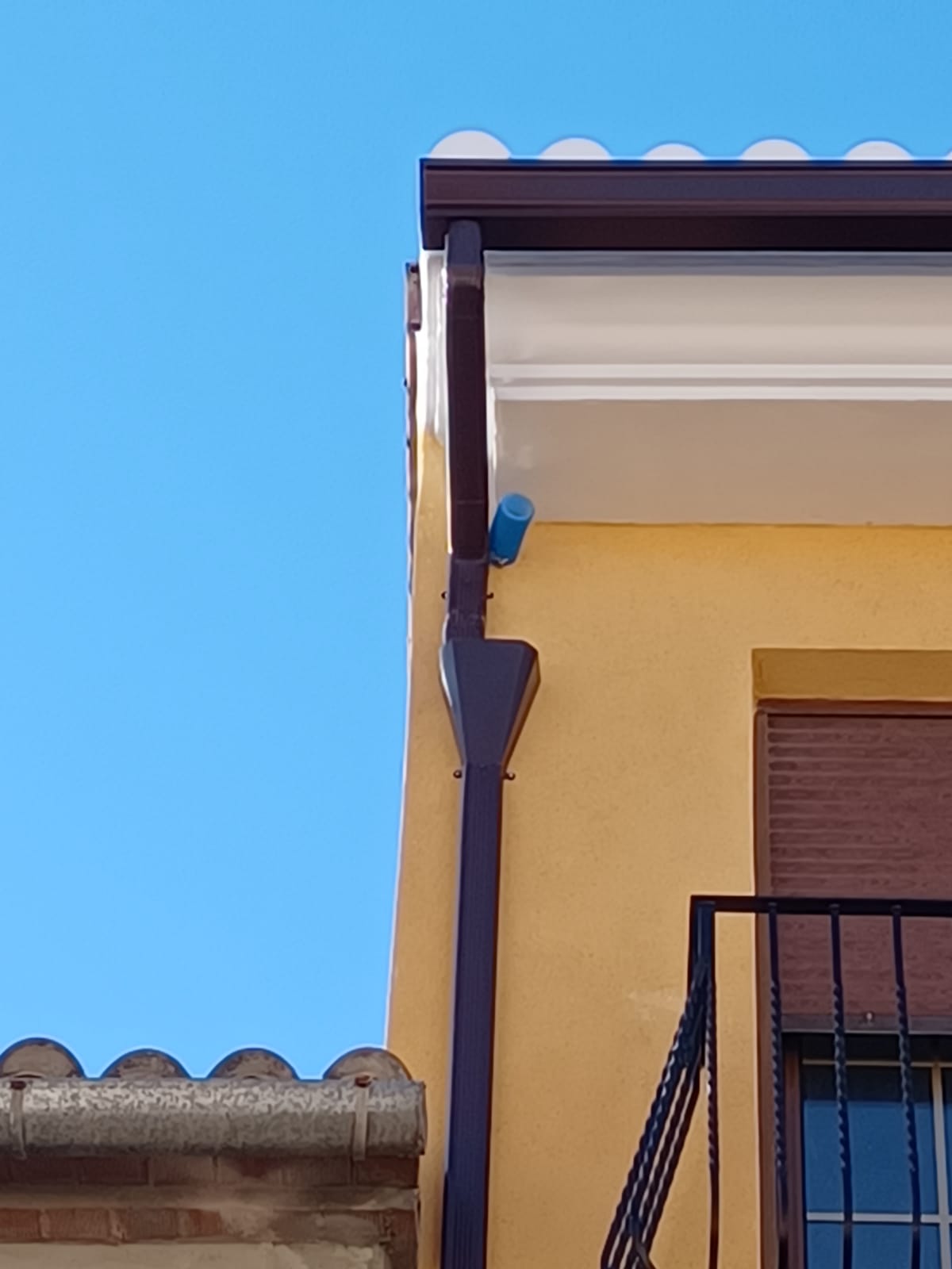 Canalón marrón con bajante en fachada amarilla instalado por CanalVal