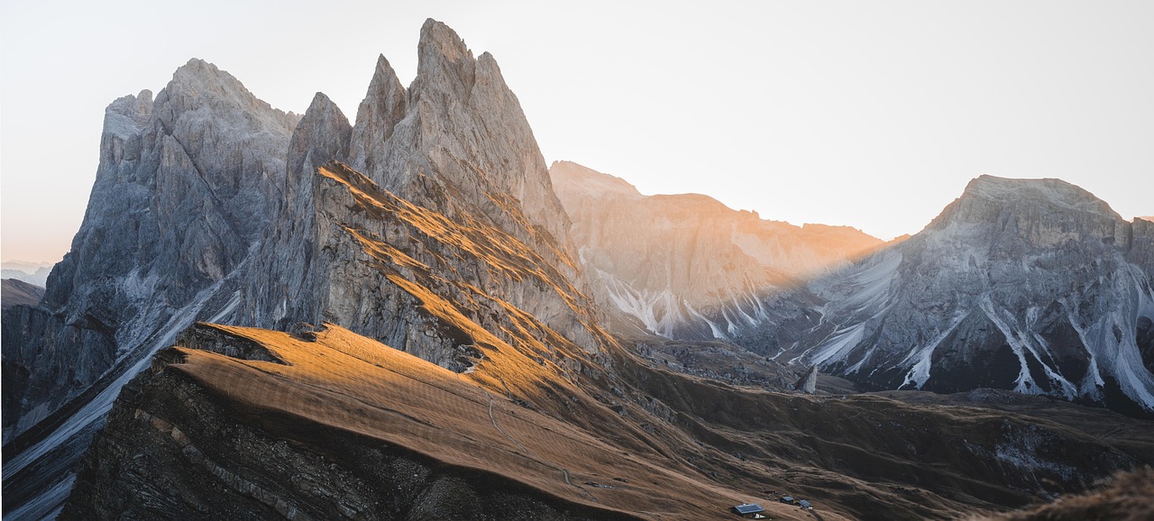Dolomite Spires The iconic jagged spires of the Dolomites illuminated by warm sunset light, with sharp rocky peaks casting long shadows across golden alpine meadows, exemplifying dramatic mountain architecture.