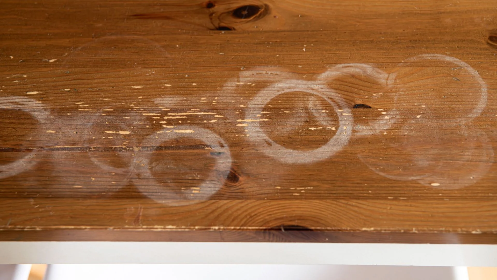 Multiple white heat rings and water marks on light oak wood table surface showing common damage pattern