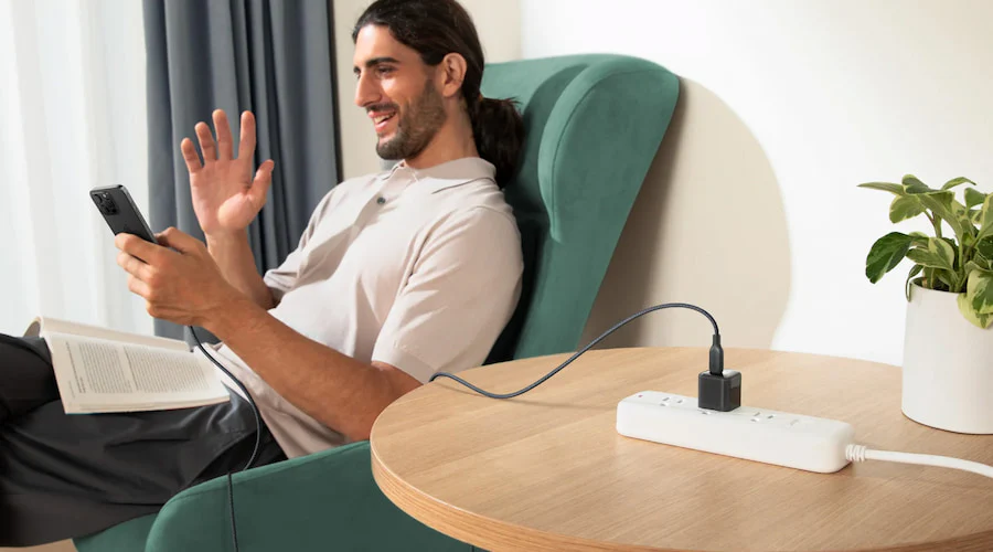 Person relaxing while phone charges on desk with cable and power strip