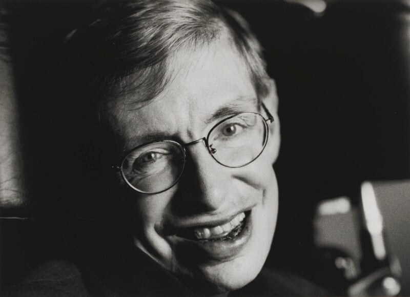 Retrato de Stephen Hawking sorrindo, usando óculos, em foto em preto e branco