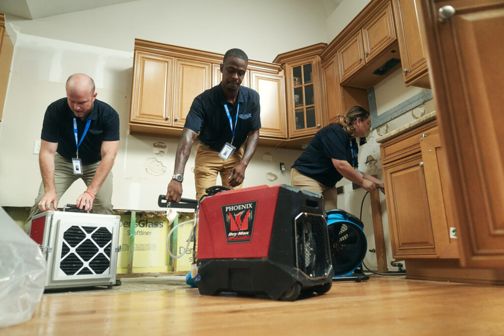 Water damage restoration technicians setting up commercial drying equipment in a flooded kitchen
