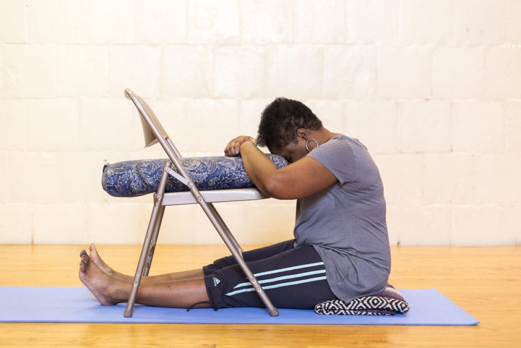 Person doing restorative yoga pose with chair support for joint comfort