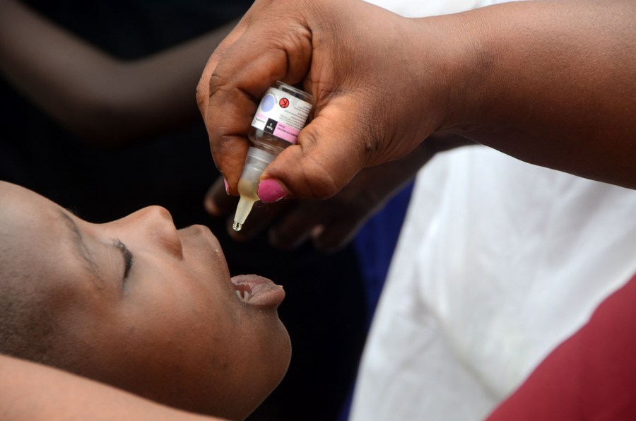 Healthcare worker administering oral polio vaccine to child in Africa