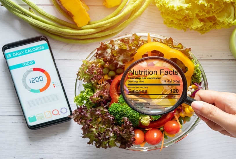 Person examining nutrition facts label on fresh salad with smartphone calorie tracker