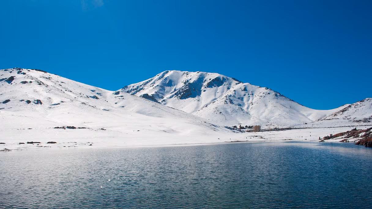 بحيرة جبلية في الأطlas المغربي محاطة بالثلوج والقمم البيضاء
