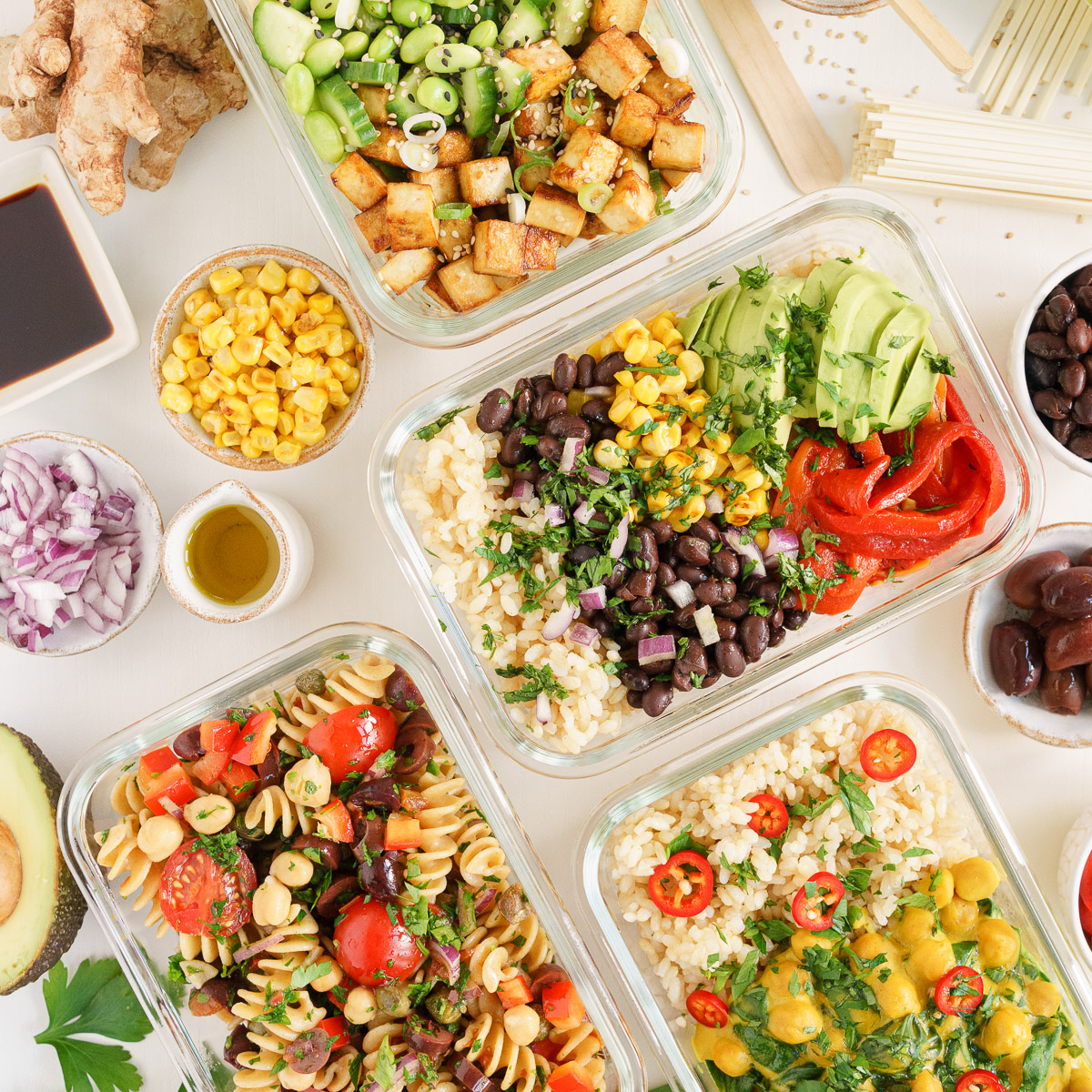 Four colorful vegan meal prep bowls with tofu, beans, grains, and fresh vegetables