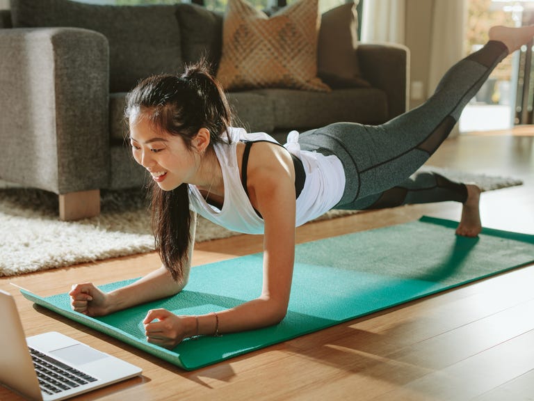 Woman doing plank exercise on yoga mat at home with laptop
