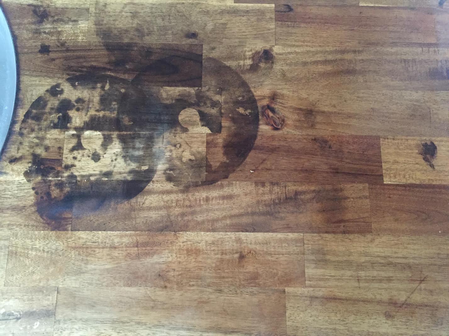 Close up of rancid coconut oil damage showing yellow sticky residue and dark oxidation spots on wood cutting board