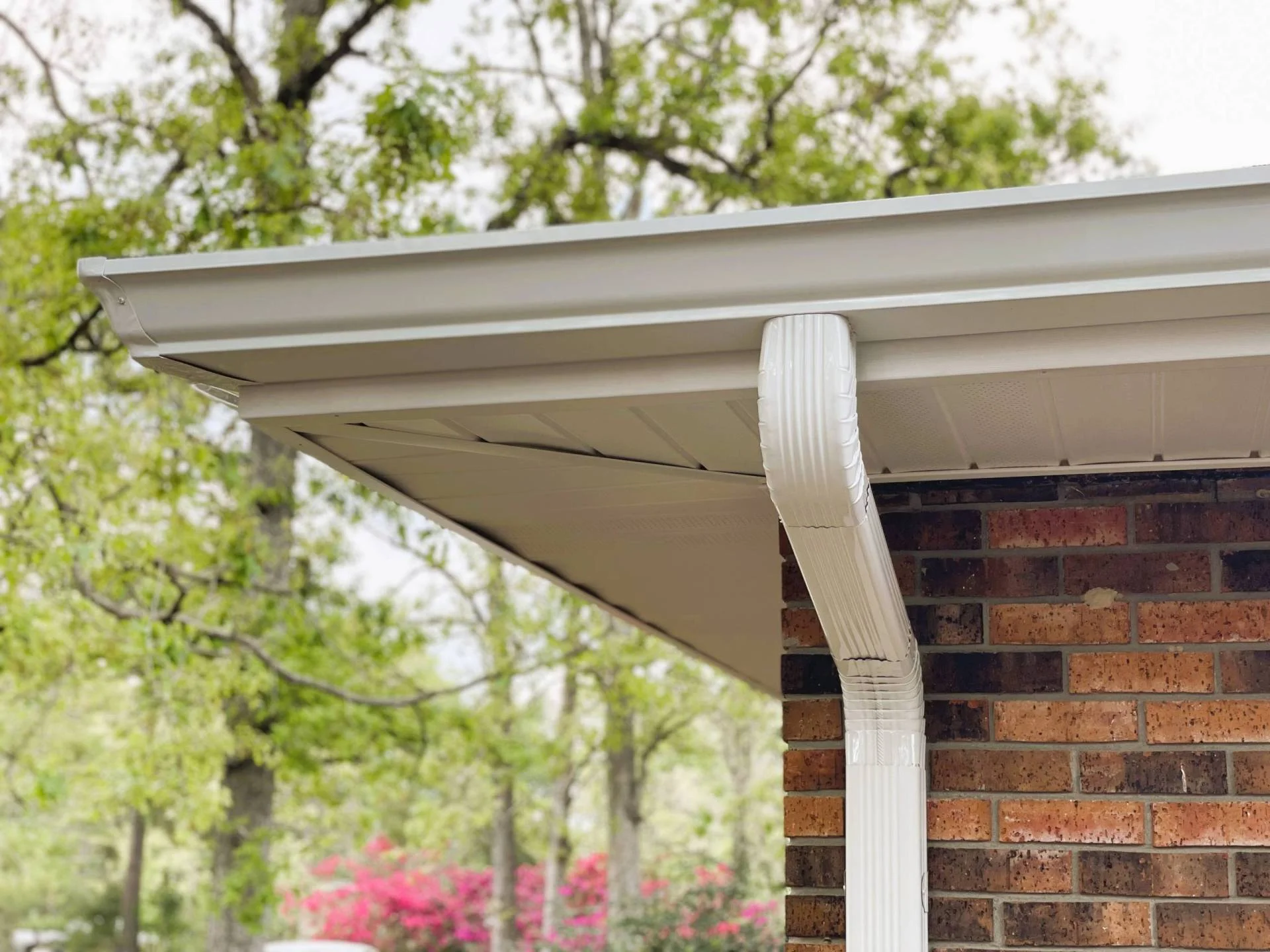 Clean white gutter and downspout on a brick house