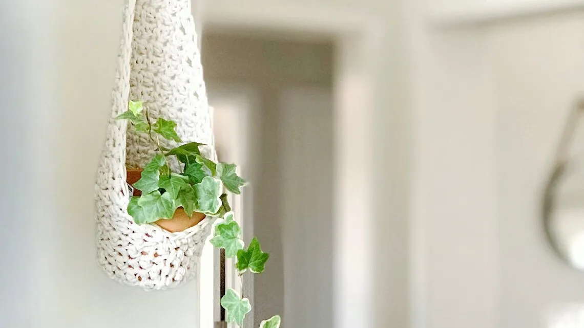 White boho crochet hanging planter pod with trailing ivy in bright room