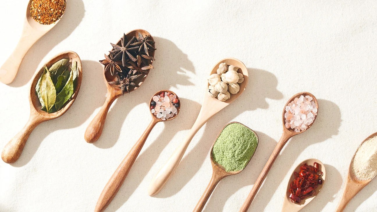 Natural home remedies in wooden spoons including herbs and spices