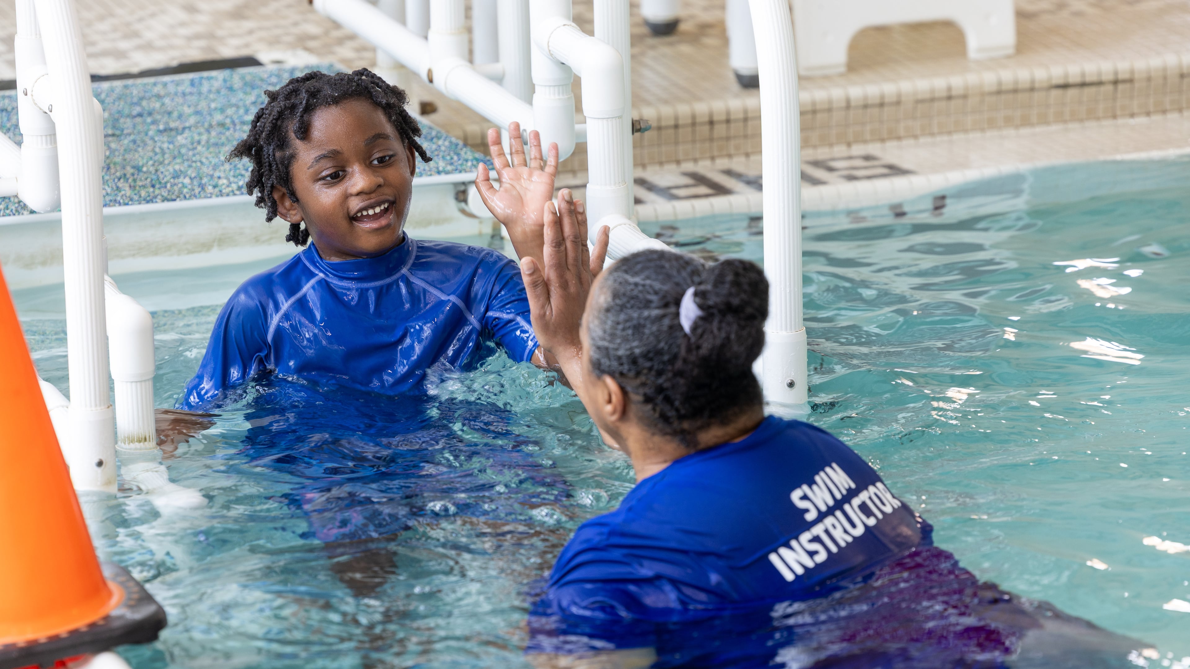 Swim instructor giving high-five to child with disability during adaptive swim lesson