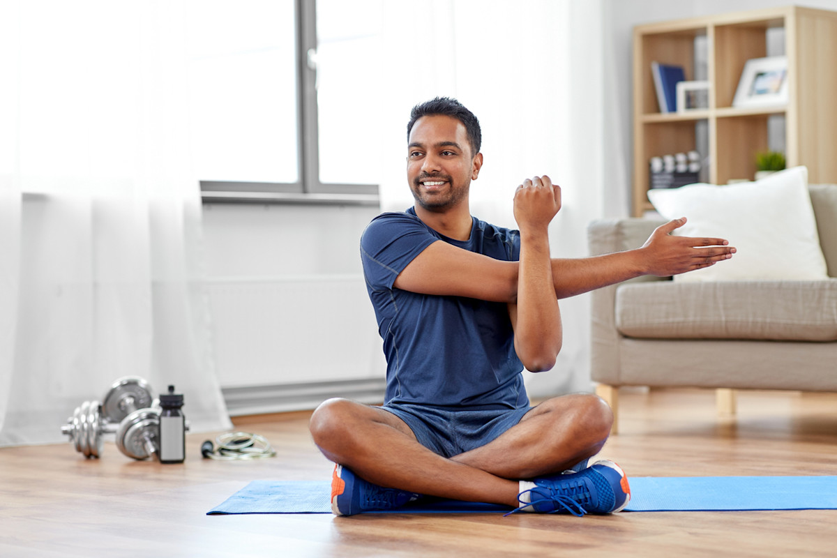 Beginner stretching and warm-up routine for home fitness workout Man stretching on a yoga mat in a bright home living room with dumbbells nearby