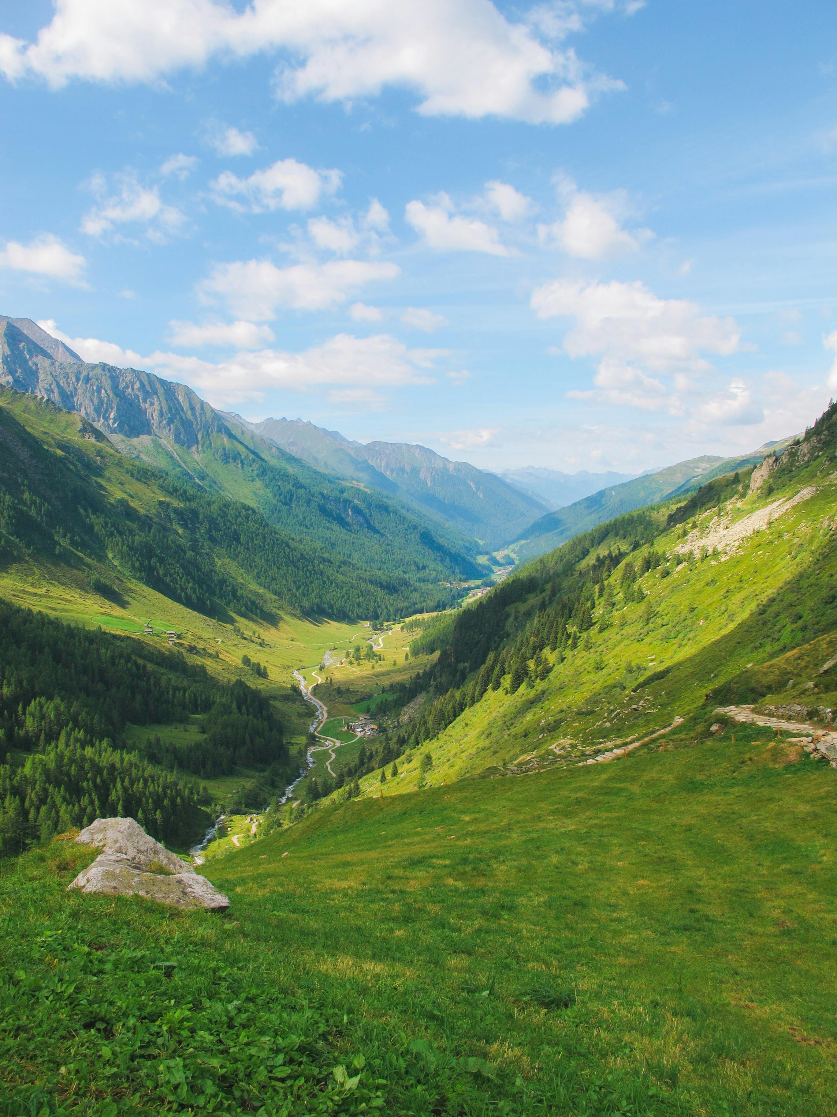 Alpine Valley Corridor A deep alpine valley carved between towering mountain ranges, with a winding river and road cutting through verdant meadows, illustrating the dramatic elevation changes of glacial terrain.