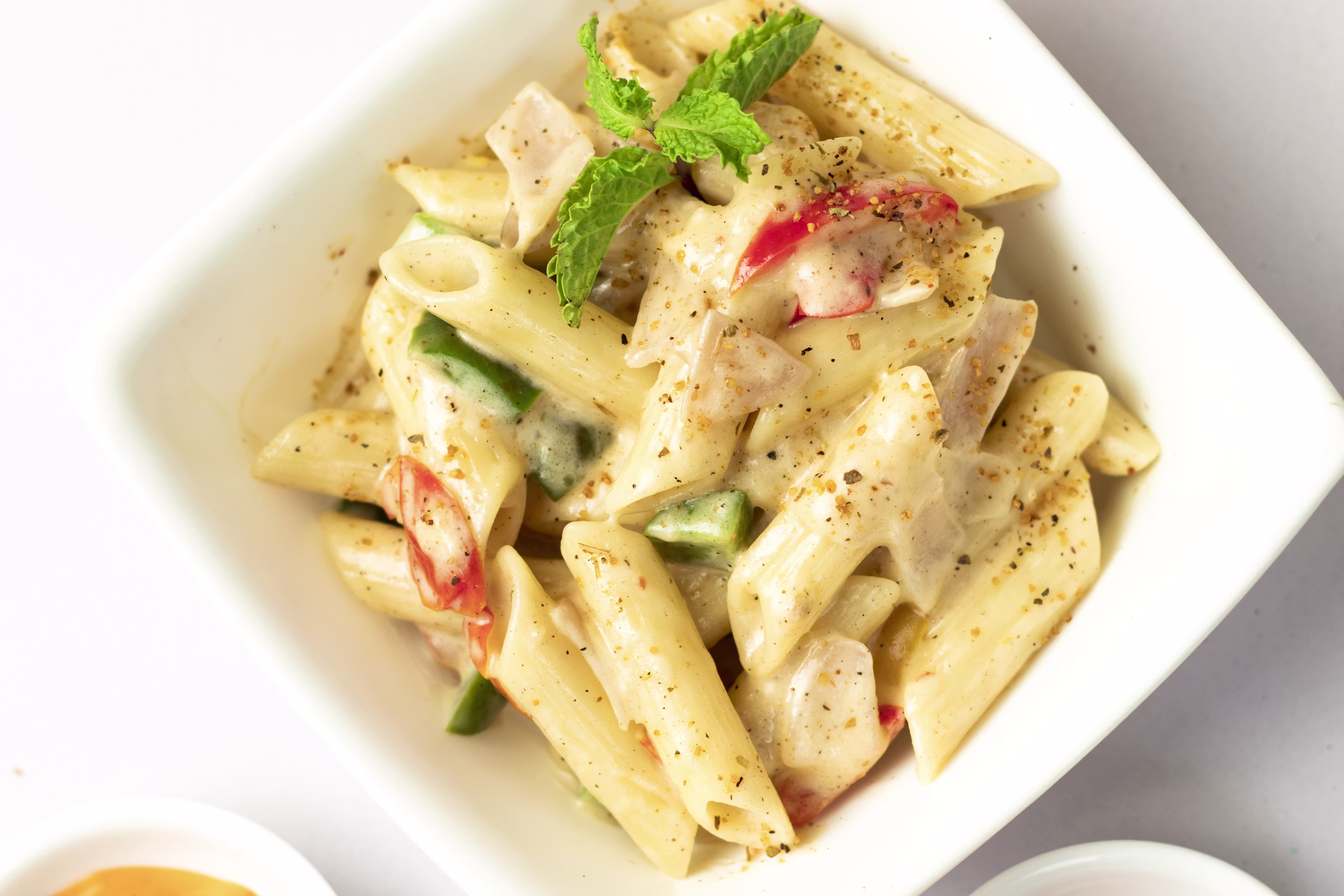 Creamy chicken pasta penne with vegetables herbs in white bowl