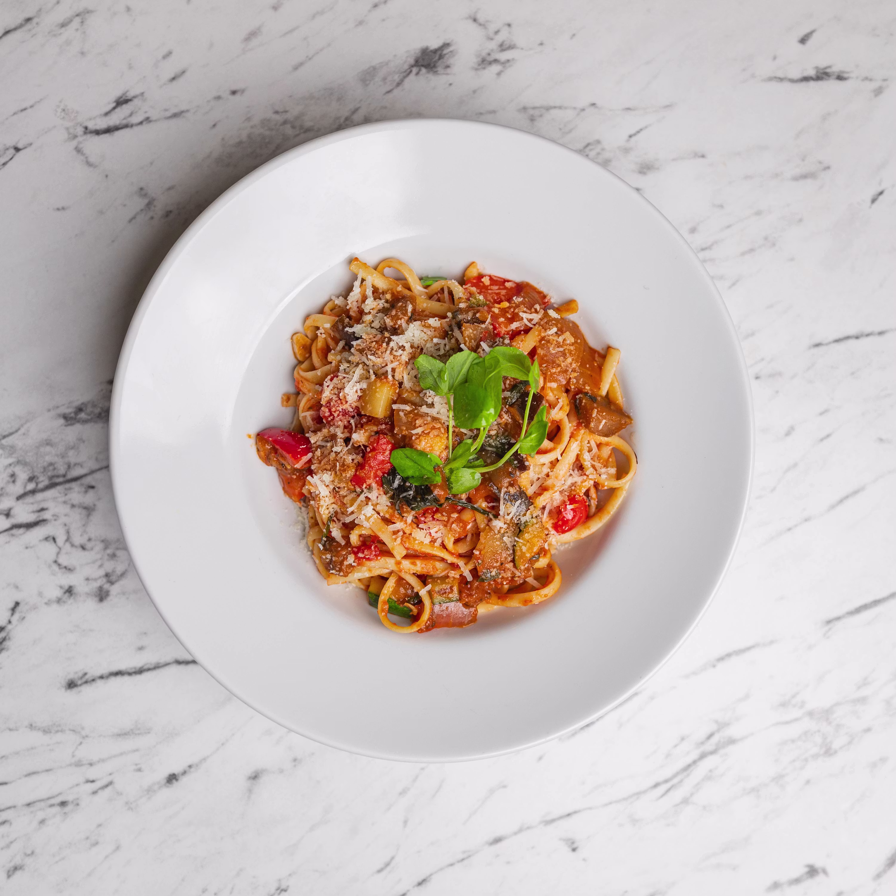 Pasta dish with tomato sauce parmesan basil on white marble plate