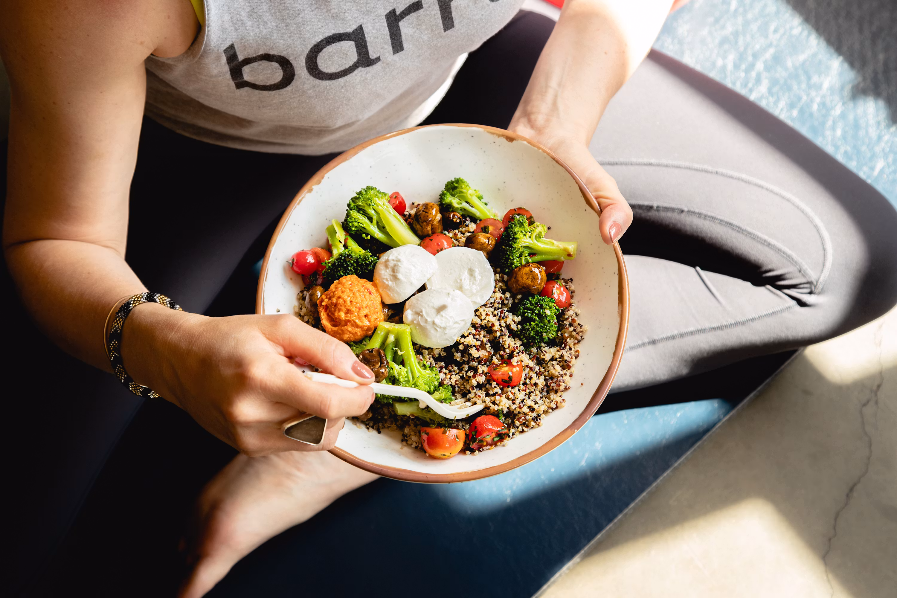 Person holding healthy quinoa bowl with broccoli tomatoes poached eggs