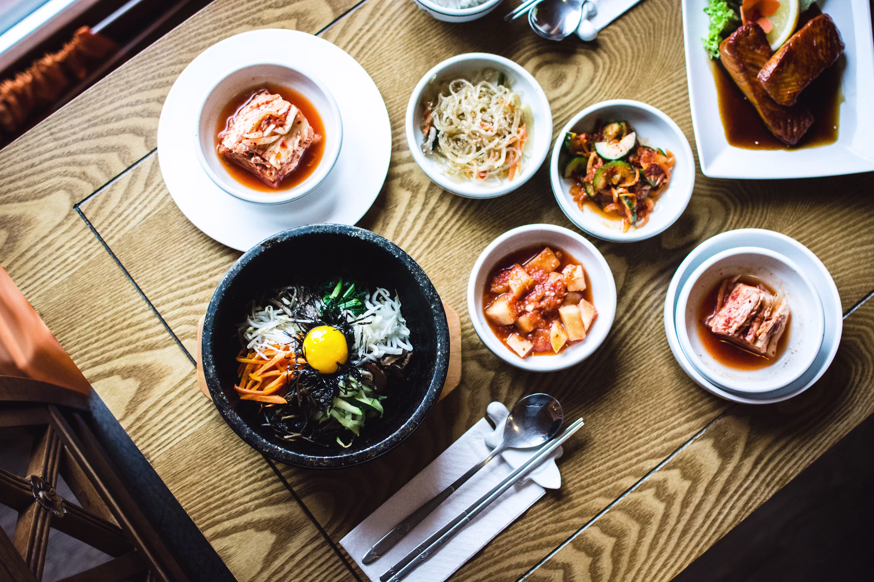 Korean bibimbap and banchan side dishes spread on wooden table
