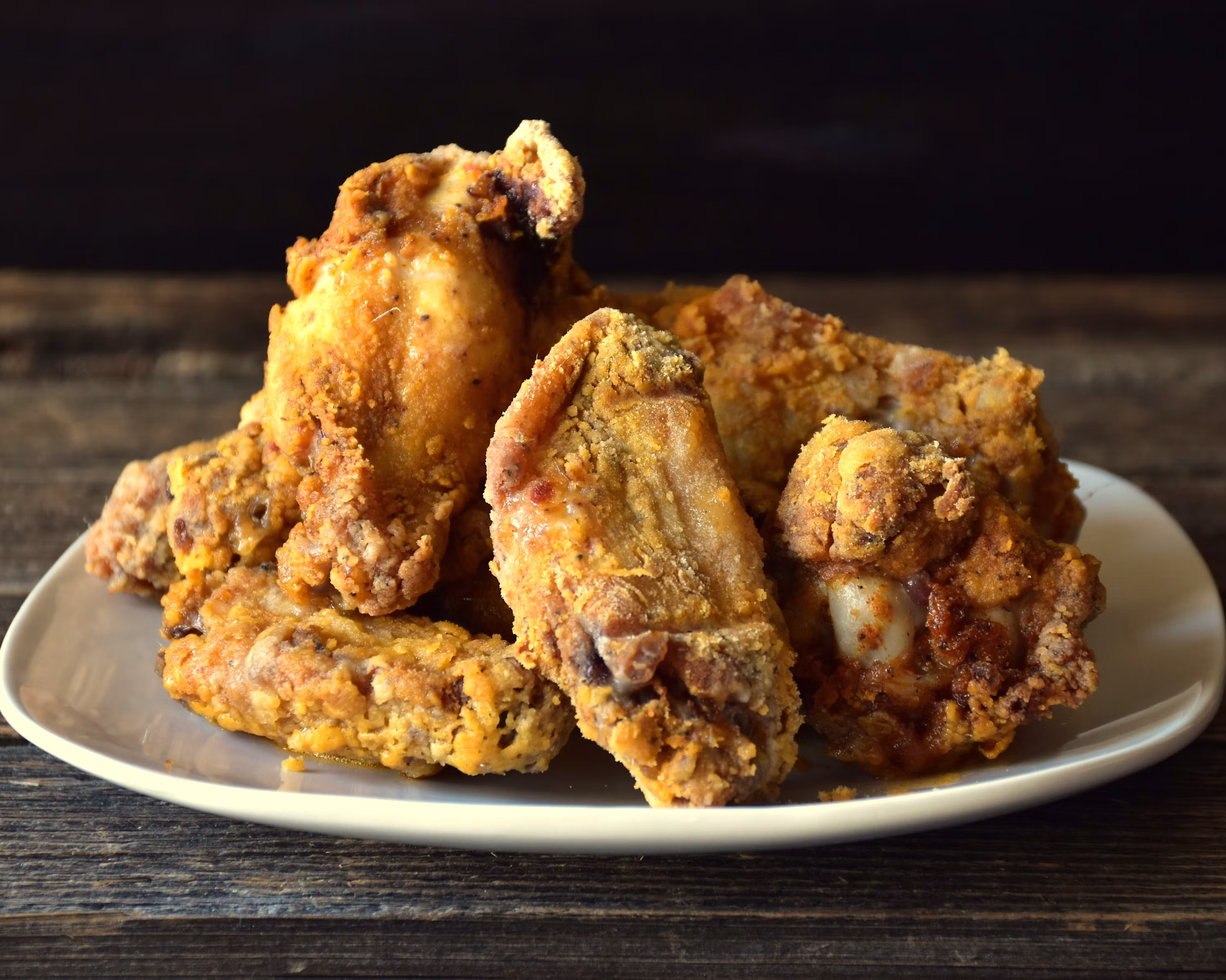 Crispy fried chicken wings stacked on white plate dark background