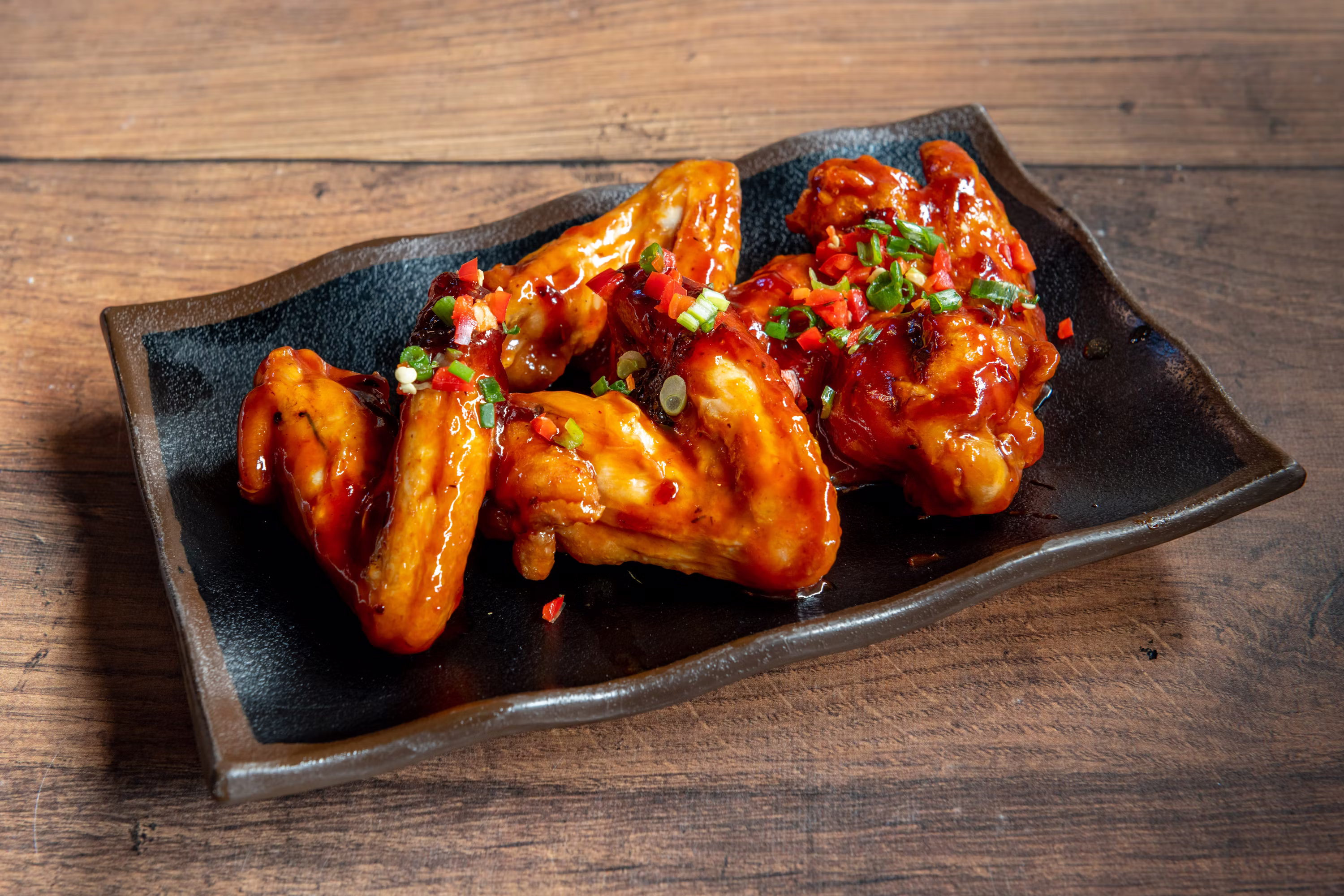 Buffalo chicken wings with green onions and chili on black plate