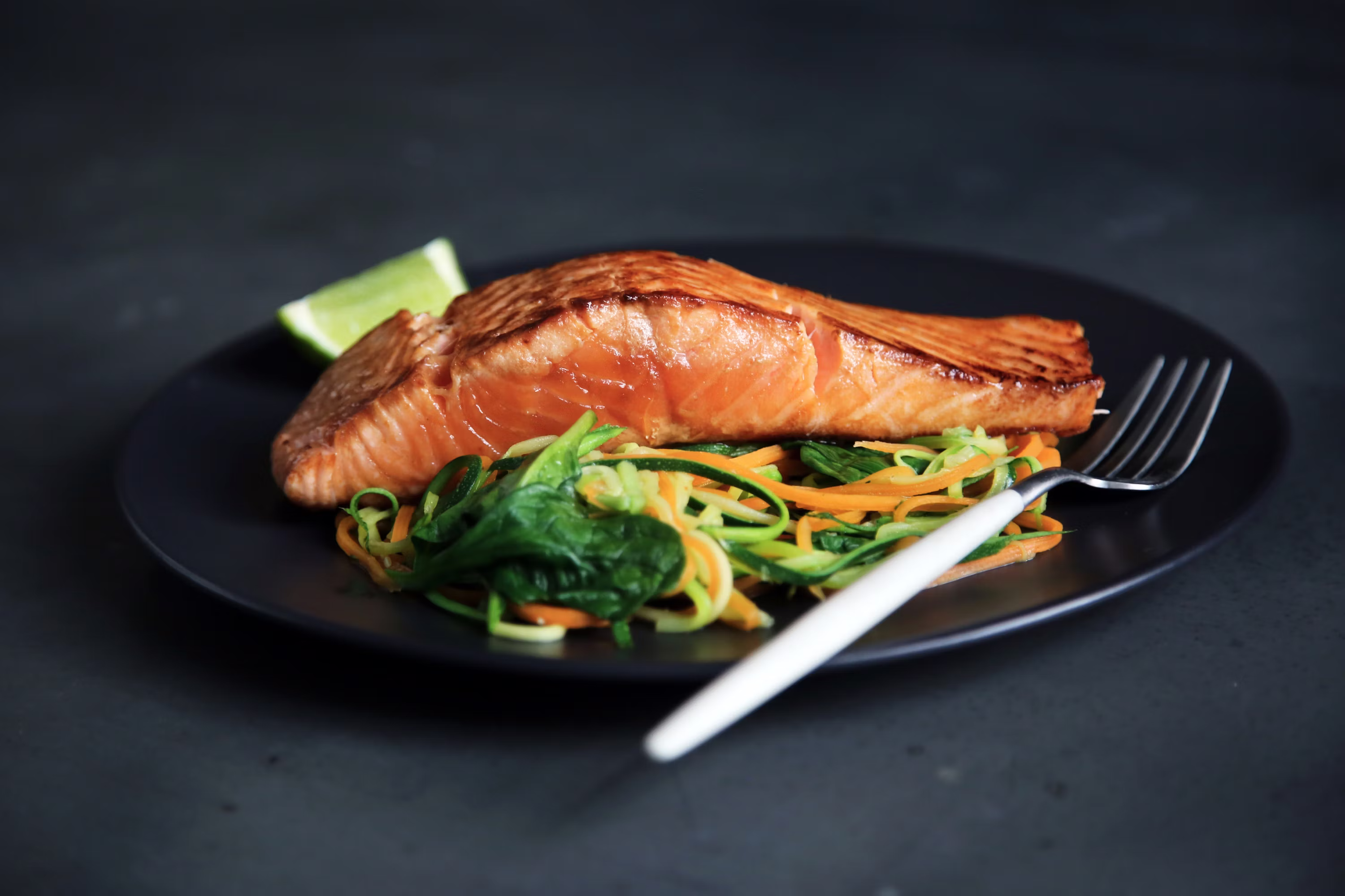 Grilled salmon fillet with spiralized vegetables and lime on black plate