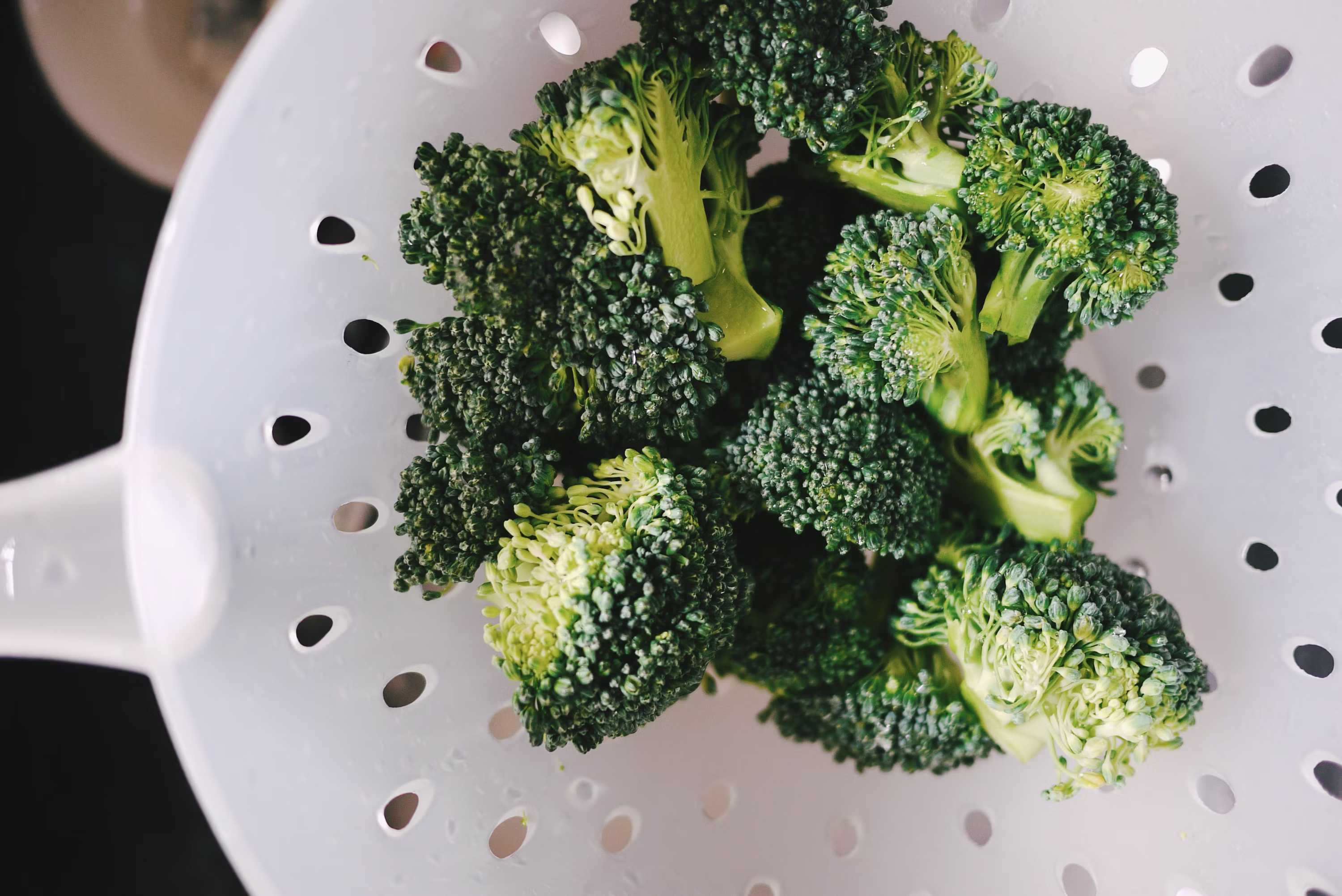 Fresh green broccoli florets in white colander overhead view