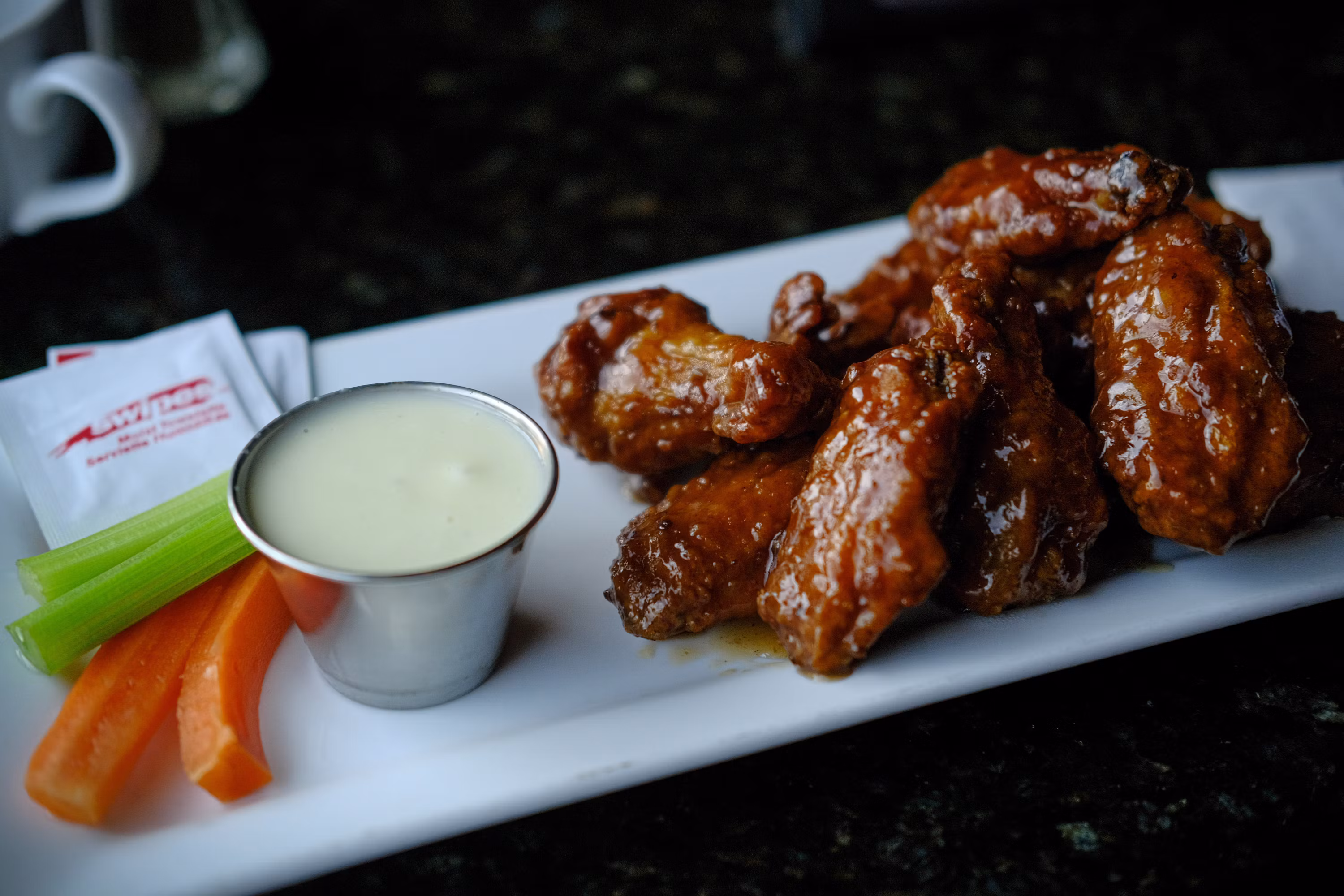 Glazed chicken wings with dipping sauce celery and carrots on white plate
