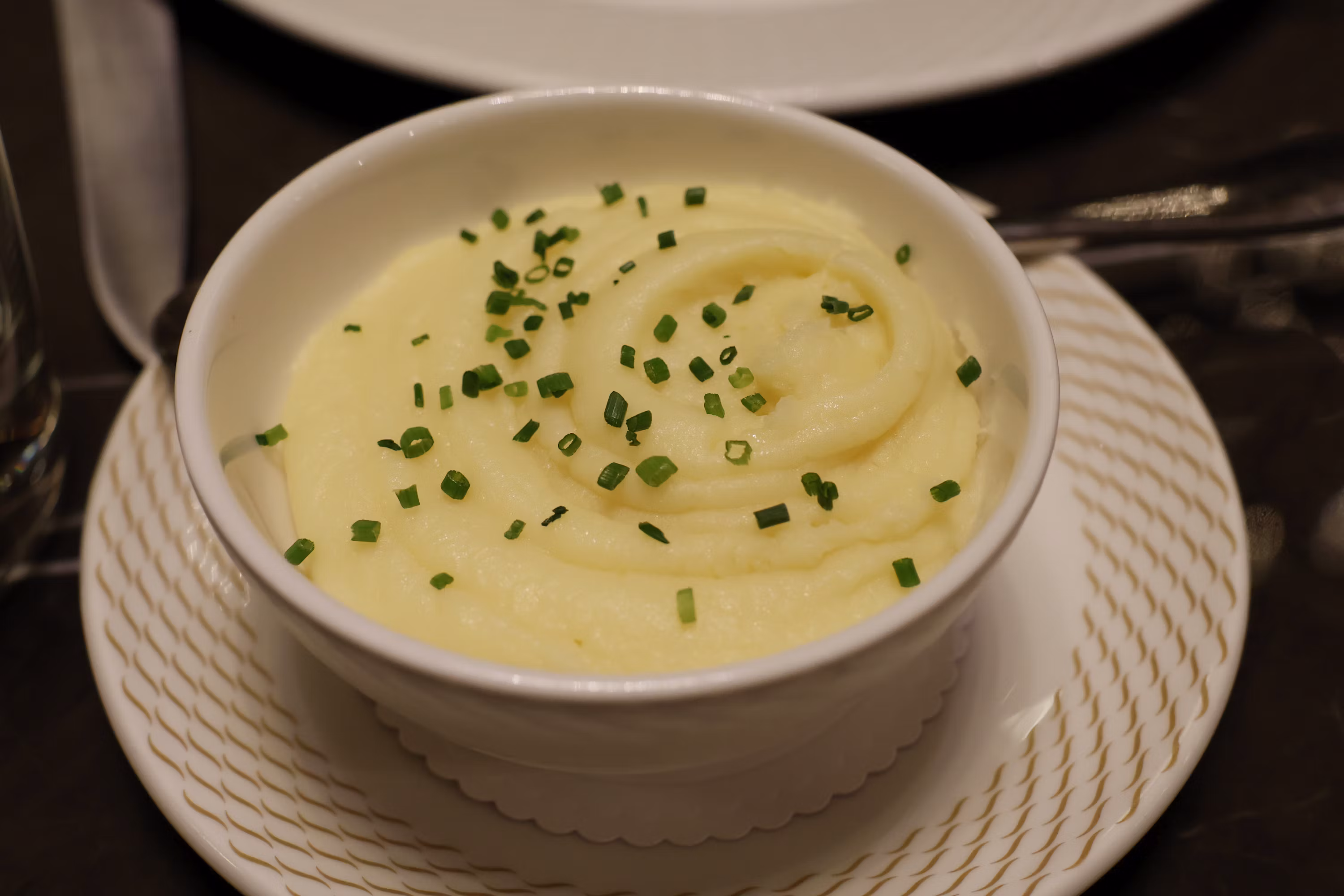 Creamy mashed potatoes in white bowl topped with chives