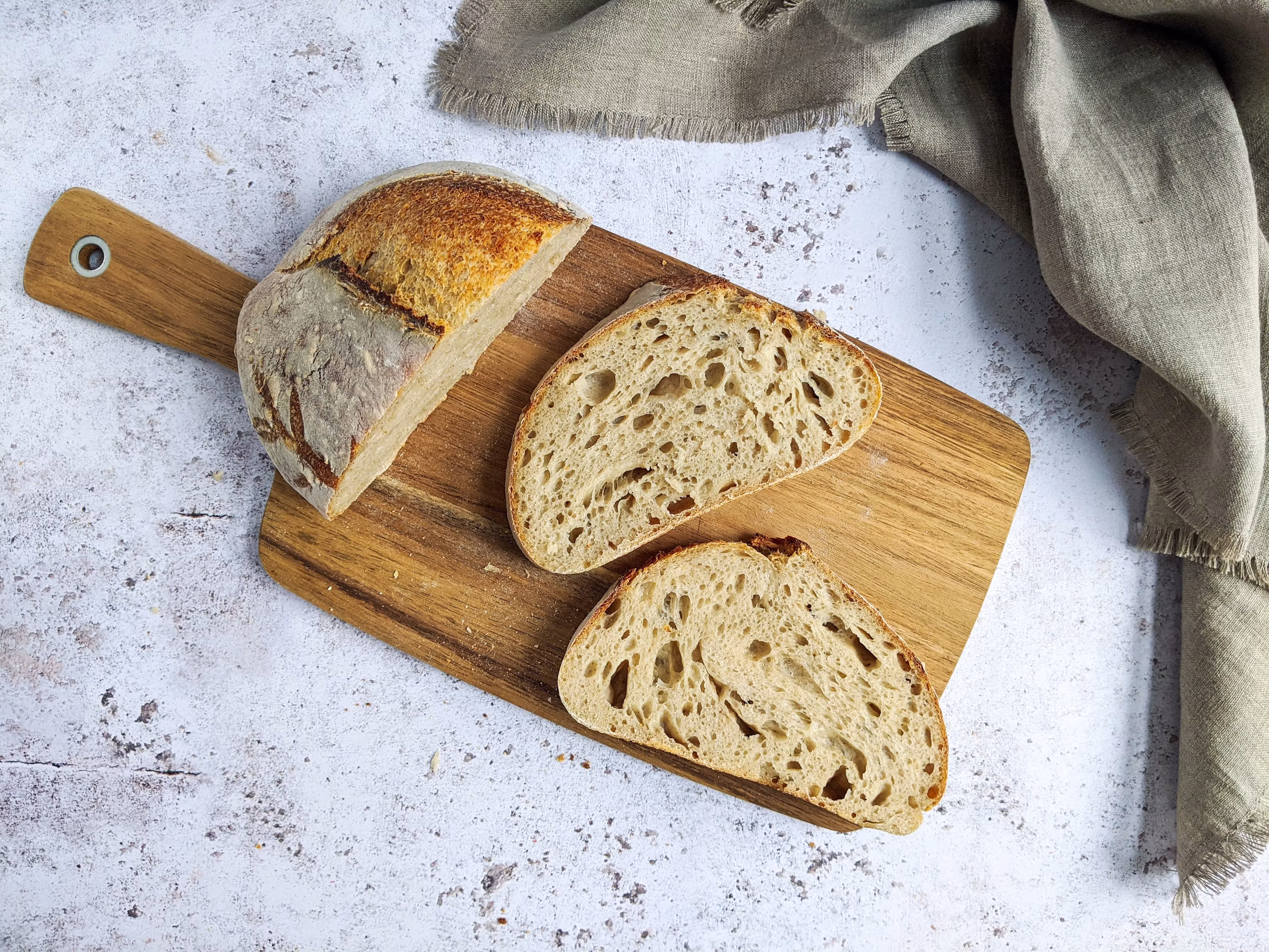 Sliced sourdough bread on wooden cutting board with linen napkin