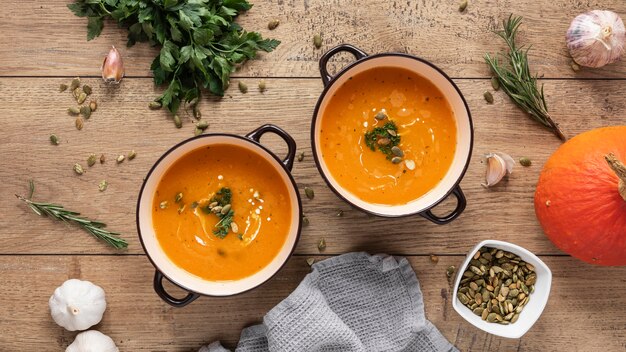 Flat lay of pumpkin soup ingredients including fresh pumpkin, herbs, garlic and spices on a warm wooden surface