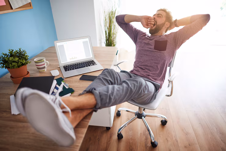 Homem relaxado em cadeira de escritório com os pés na mesa, representando bem-estar no trabalho