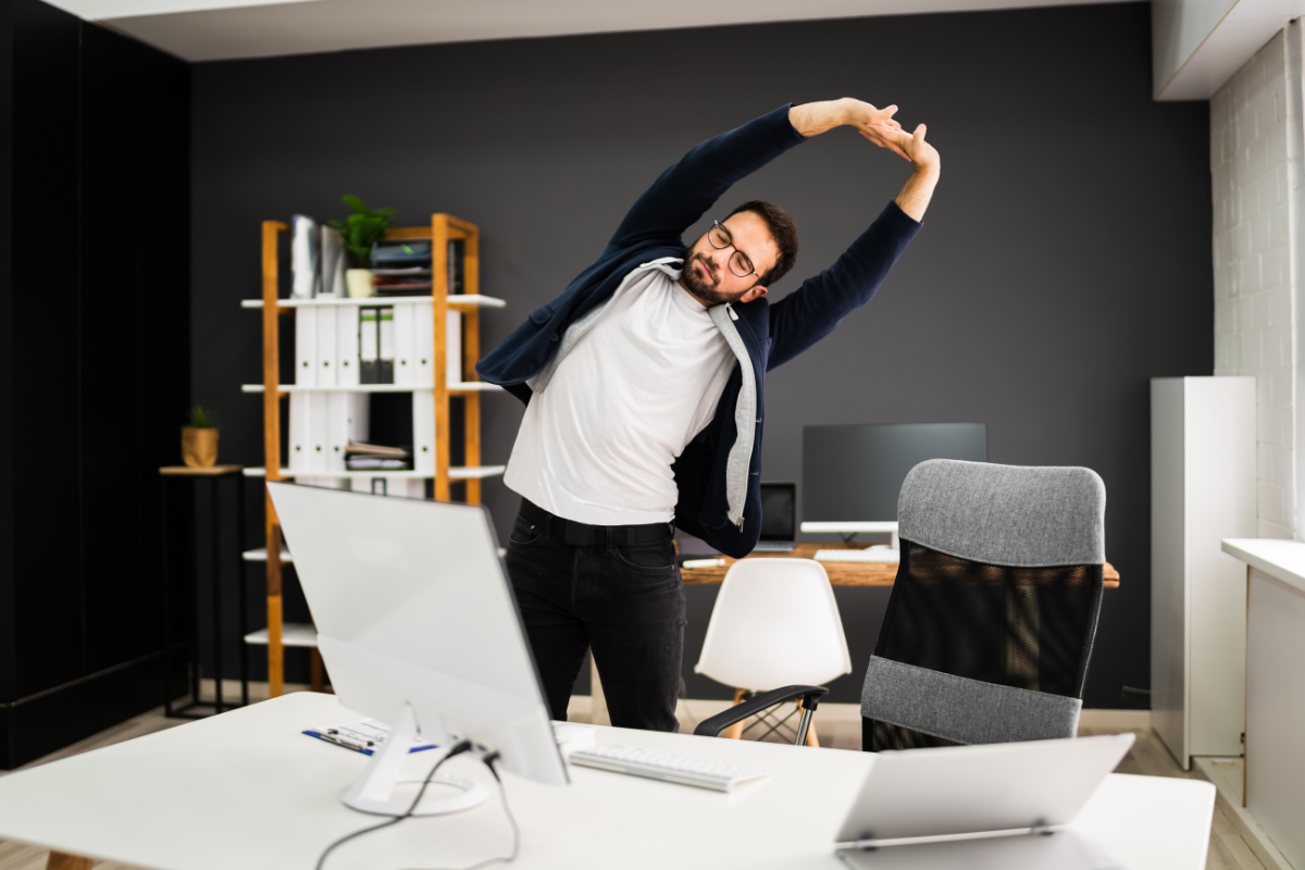 Office worker standing and stretching at desk to break up sitting time