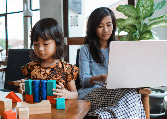 Toddler playing with blocks while parent works on laptop nearby
