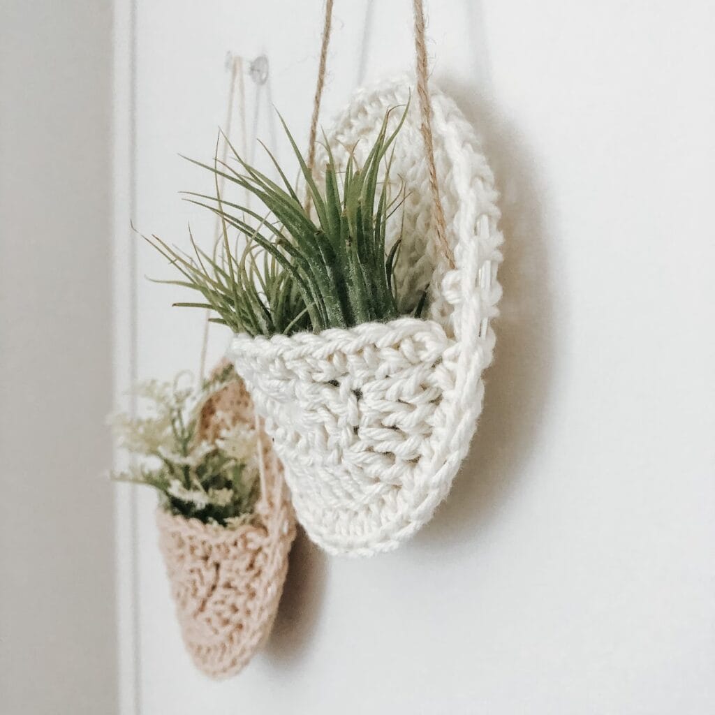Two crochet wall plant pockets with air plants hanging on white wall