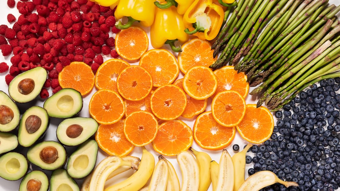 Fresh colorful fruits and vegetables including avocados, oranges, asparagus, blueberries, raspberries, and bell peppers