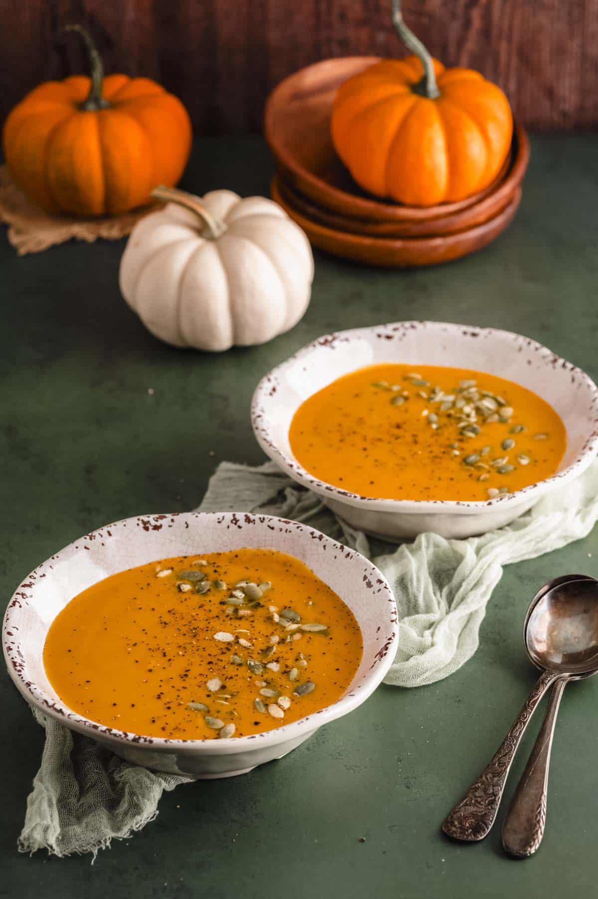 Creamy pumpkin soup in a white bowl topped with seeds and herbs, warm rustic setting