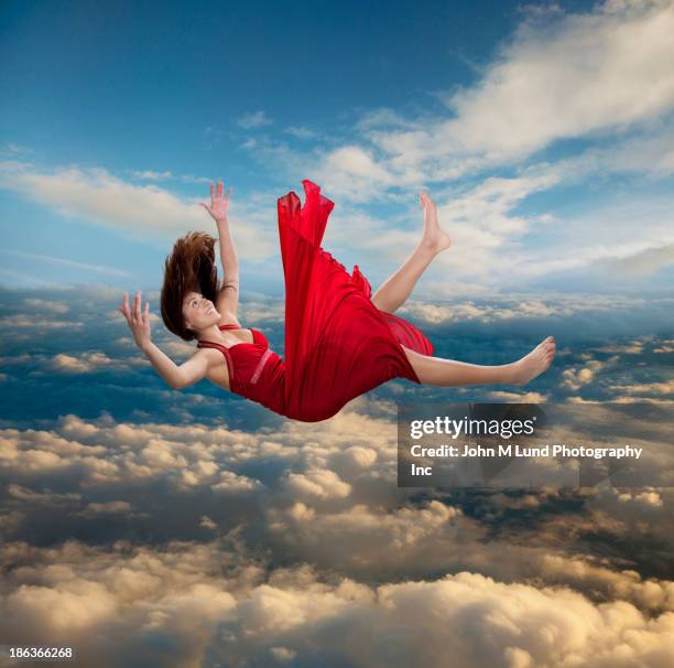Model in red dress flying through clouds