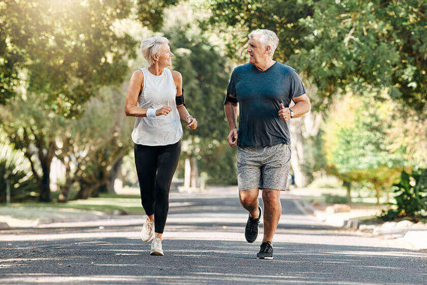 Casal de idosos ativos praticando corrida ao ar livre em parque arborizado
