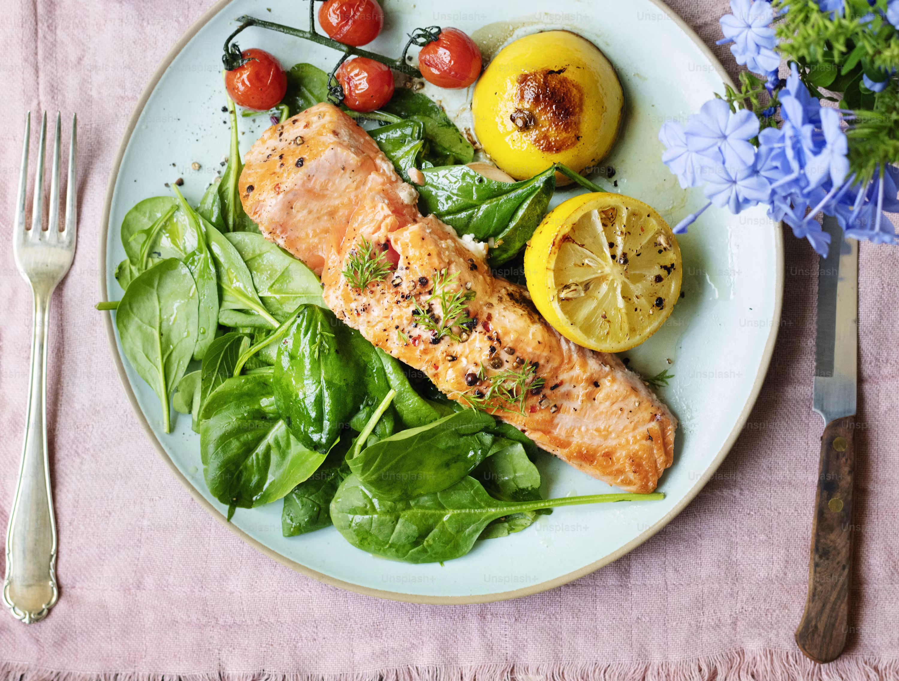 Baked salmon fillet with lemon spinach cherry tomatoes on blue plate