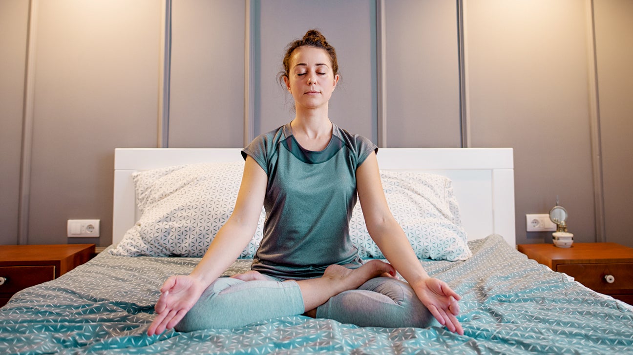 Woman meditating peacefully on bed for nighttime relaxation and better sleep