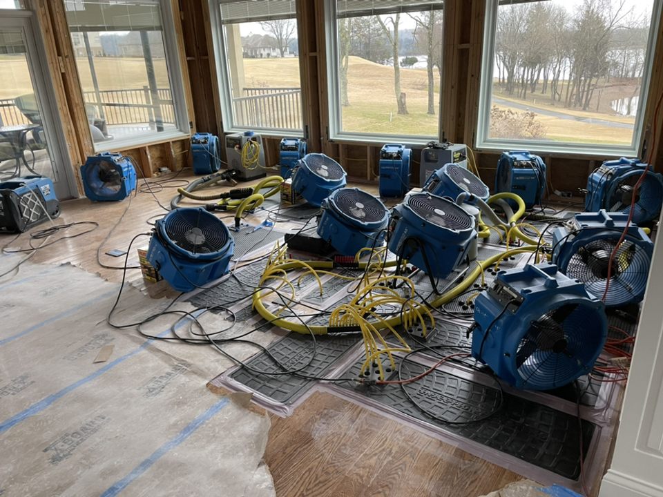 Multiple industrial air movers and dehumidifiers set up in a room for structural drying after water damage extraction
