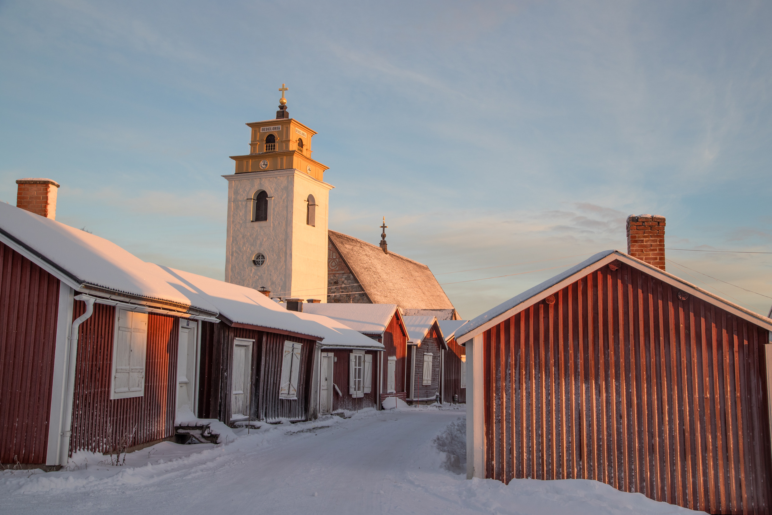 Golden winter sunrise illuminating the ochre church tower and snow-covered red wooden cottages of Gammelstad Church Town in Swedish Lapland