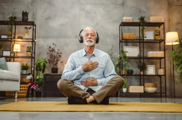 Calm mind meditation practice at home for daily wellness Senior man meditating peacefully at home with headphones in cozy living room