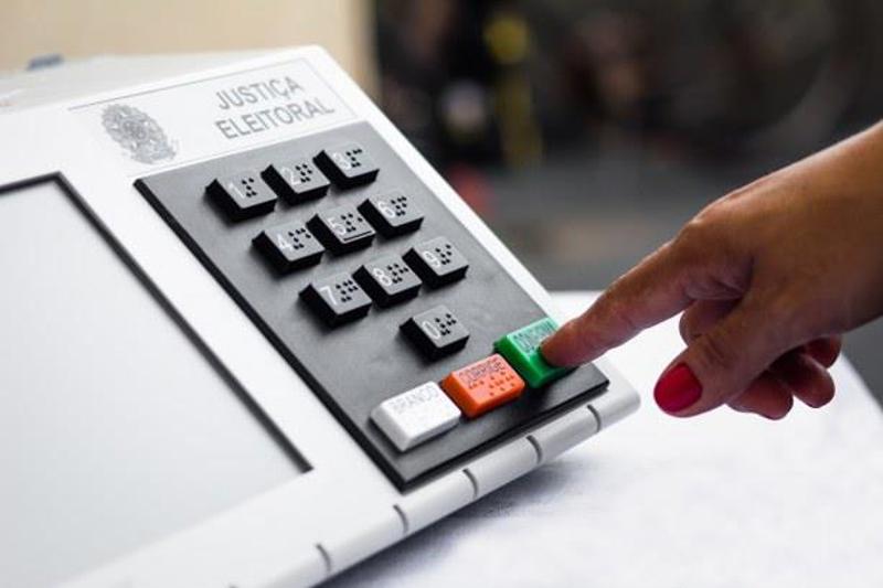 Mão de eleitor pressionando botão CONFIRMA na urna eletrônica brasileira