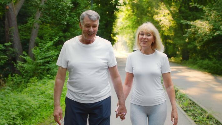 Senior couple walking hand in hand through green park for active lifestyle