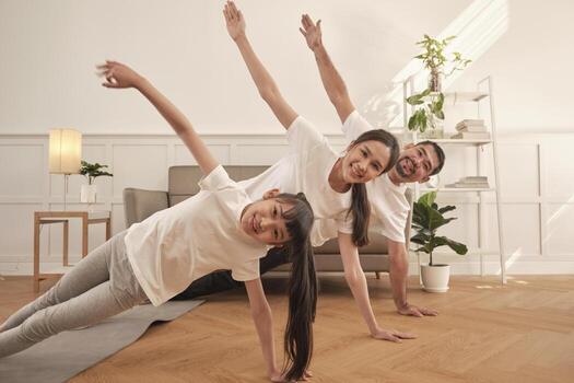 Asian Thai parents and daughter fitness training exercise and practice yoga on living room floor, lovely rowing together for health and wellness, and happy domestic home lifestyle on family weekend. 11273461 Stock
