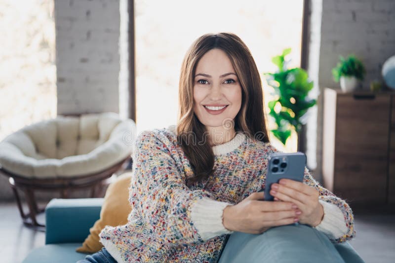 Woman relaxing on a couch at home holding her Android smartphone in a cozy living room